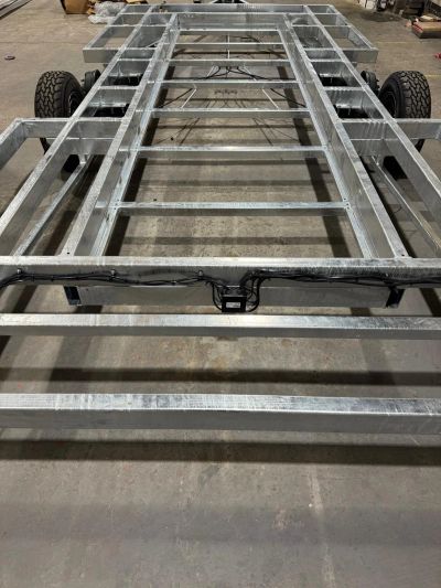 Metal frame trailer chassis with wheels.