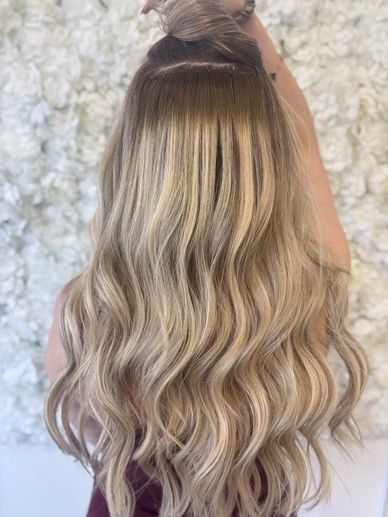 Long, wavy blonde hair with dark roots against a floral background.