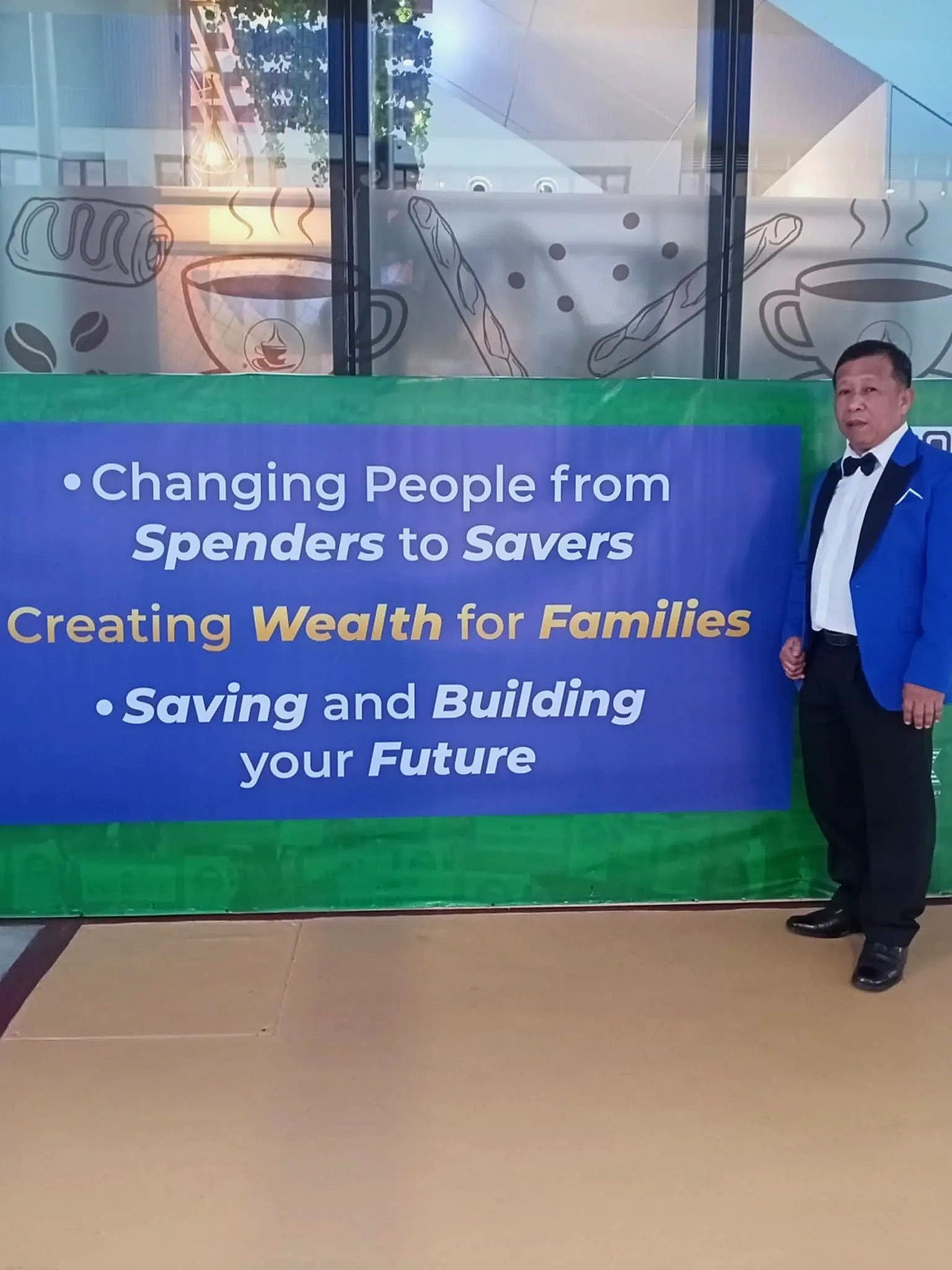 Man in blue tuxedo stands beside a banner promoting financial literacy and wealth building.