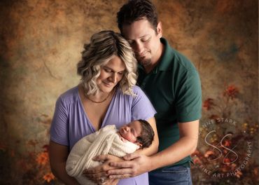 Mother and father pose with newborn, wrapped in yellow, who has full head of dark hair