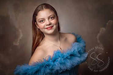Portrait: beautiful dimpled teen with long hair and blue eyes wearing off-the-shoulder couture gown