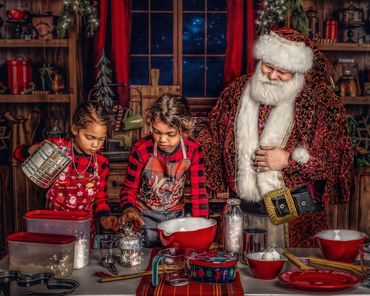 Painterly scene: Santa oversees cookie mixing with 2 little girls in his rustic Christmas kitchen