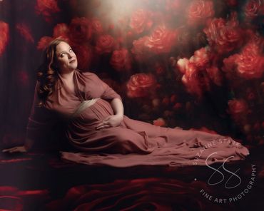 Expectant mother reclining on a backdrop of roses in a rose colored gown