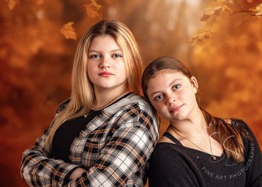2 teen girls pose in front of orange autumn leaves backdrop