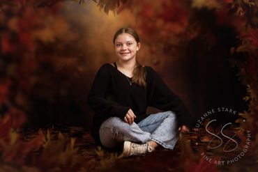 Teenaged girl in sweater and jeans seated among golden red autumn leaves backdrop