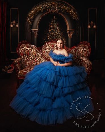 Lovely teen in long royal blue couture gown sitting on Victorian settee in elegant Christmas room