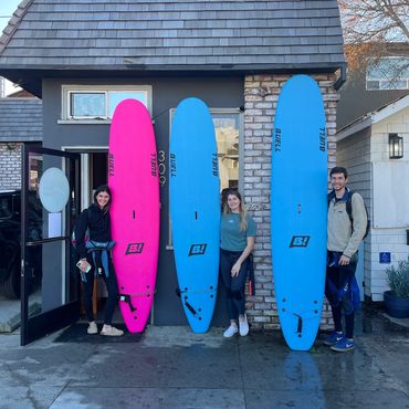 Three people posing with three surfboards in front of a building.