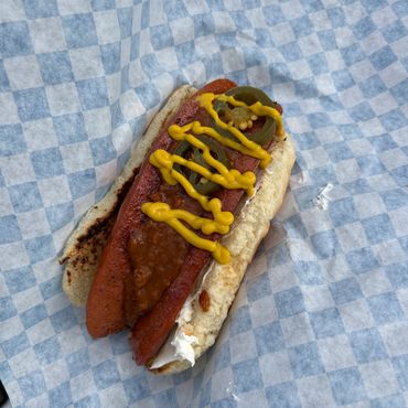 Hot dog with mustard, jalapeños, chili, and cream cheese in a bun.