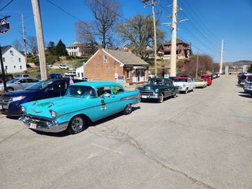 A line of vintage cars parked on a sunny street near small buildings.