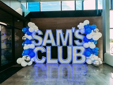 Blue and white balloon arch around illuminated SAM'S CLUB sign.
