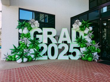 Green and white balloon arch with "GRAD 2025" sign for a graduation event.
