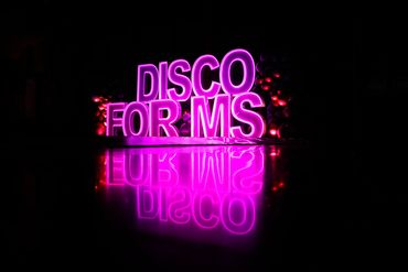 Bright pink neon sign reading "DISCO FOR MS" with reflective floor.