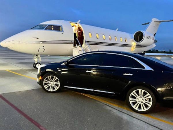 Private jet and luxury black car parked on an airport tarmac at dusk.