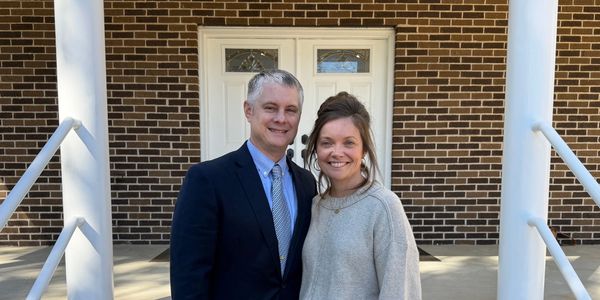 A smiling couple standing outside a brick building.