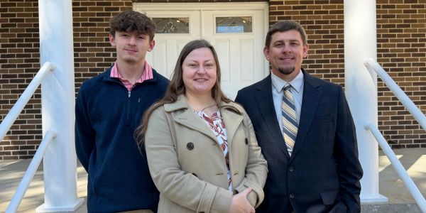Three people standing outside a brick building.