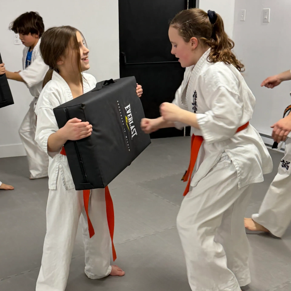 Two children practicing martial arts with one holding a training pad.