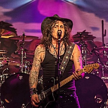 Tattooed guitarist with a cowboy hat performing on stage.
