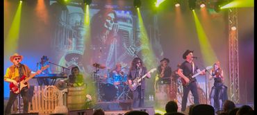 A country rock band performs on stage with spooky Halloween decorations and vibrant lighting.
