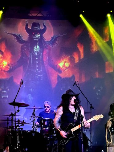Rock band performs with fiery demonic backdrop and dramatic lighting.