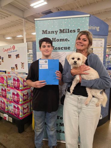 Woman holding a white dog and a boy holding a folder in a pet store.