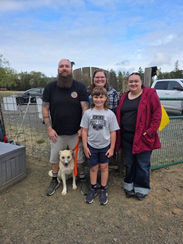Group of people and a dog smiling outdoors.