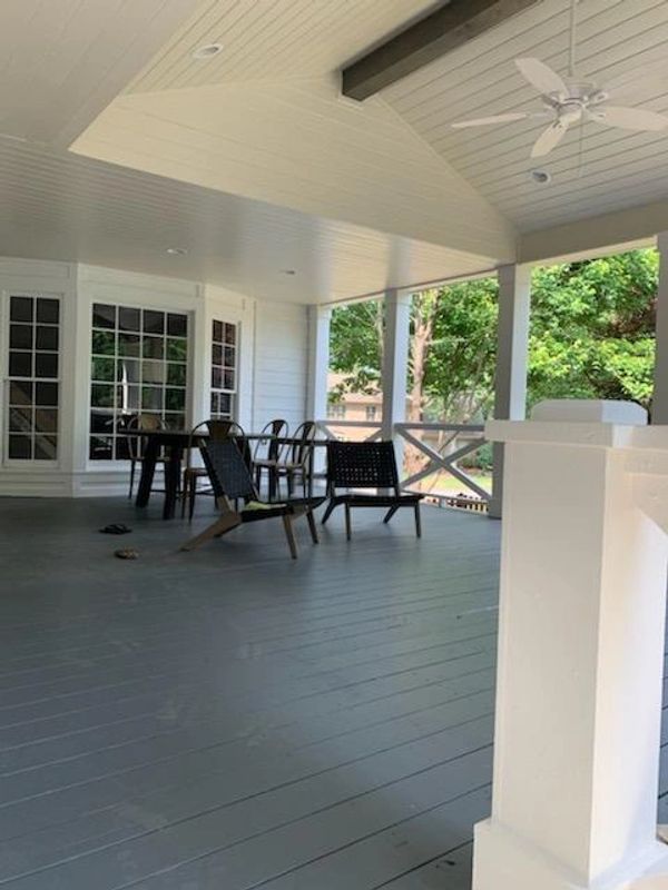 A spacious porch with chairs and a table under a ceiling fan.