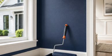 Paint roller resting against a navy blue wall inside a room.