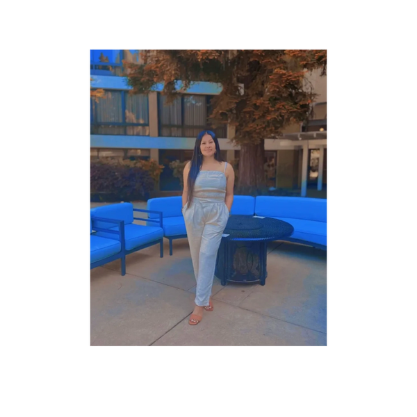 Woman posing outdoors near blue cushioned seating and a tree.