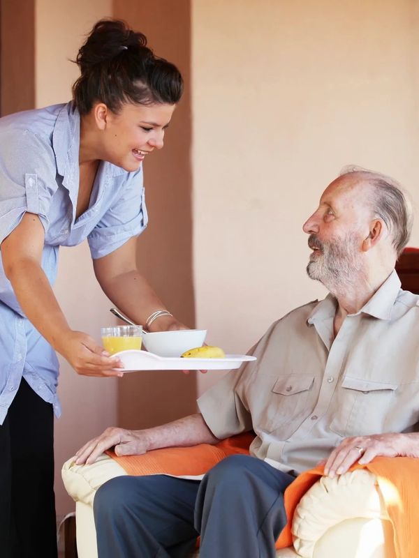 Carer serving food to an elderly man