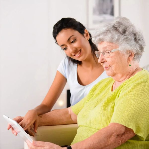 Elderly woman being taught by a carer how to use the tablet