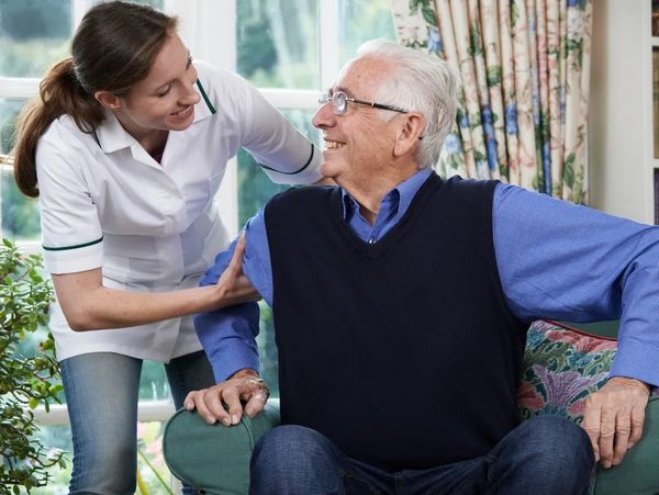 Carer helping an elderly man to get up from the sofa