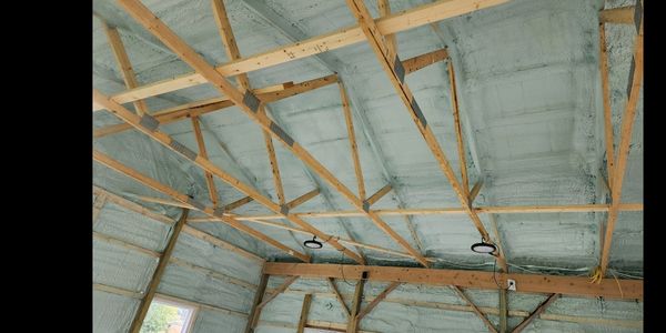 Interior roof framework with spray foam insulation and wooden beams.
