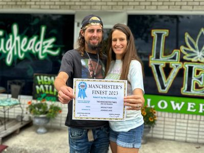 A happy couple proudly holding a "Manchester's Finest 2023" certificate outdoors.