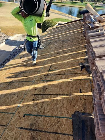 A worker carrying roofing materials on a wooden roof under construction.