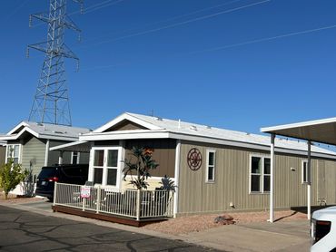 A beige manufactured home with a small porch and a clear blue sky.