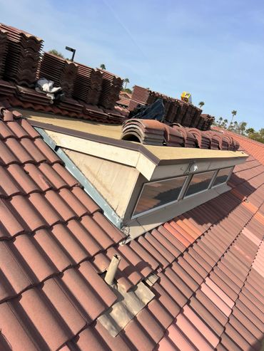 Tile roof under repair with stacks of tiles and a dormer window.