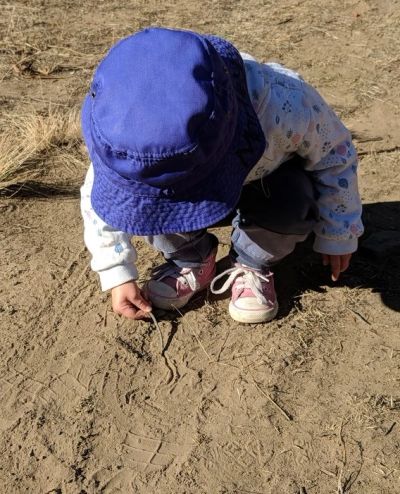 Child in blue hat drawing in dirt.