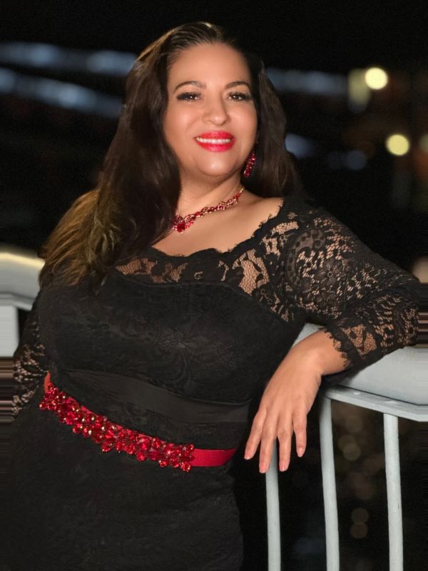 Smiling woman in black lace dress with red accessories at night.