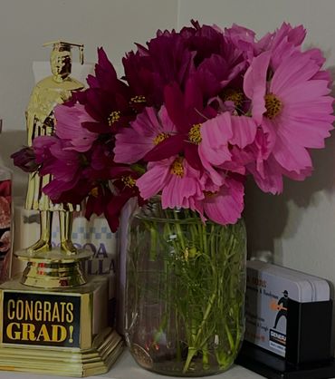 A congratulatory graduation trophy next to a vase of pink flowers.