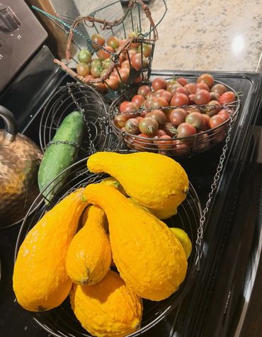 Fresh yellow squash, cherry tomatoes, and a cucumber on a kitchen stove.