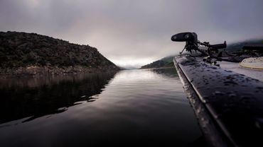 Barca da pesca ferma sul lago all’alba, con atmosfera calma e riflessi sull’acqua.