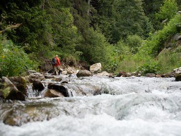 Persona che risale un torrente in montagna, immersa nella natura tra rocce e acqua corrente.