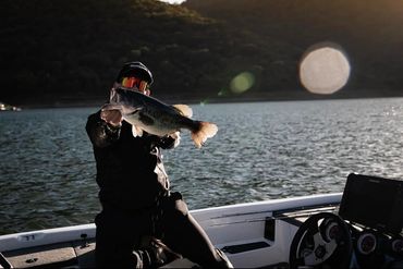 Pescatore in barca che mostra un pesce appena catturato al tramonto, momento finale del racconto outdoor.