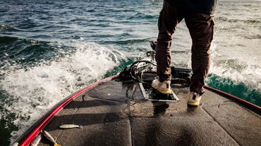 Persona in piedi su barca durante una sessione di pesca, con l’acqua in movimento.