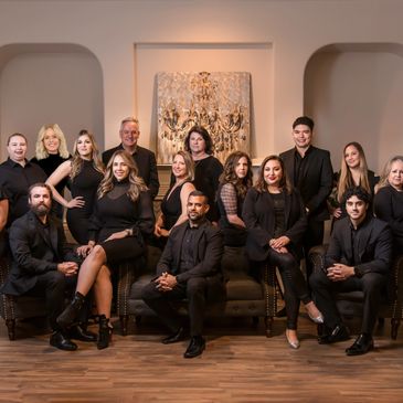 A large group of professionally dressed people posing indoors on sofas and floor.