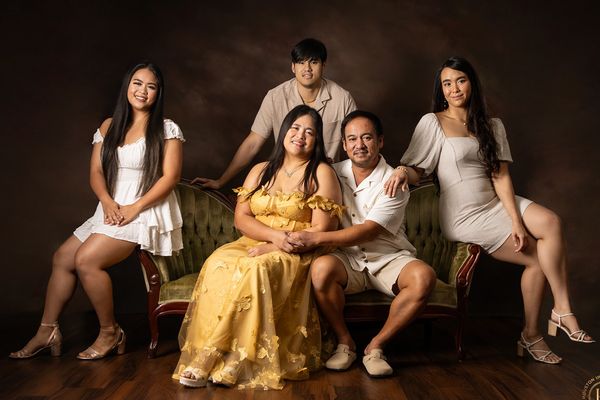 A family of five posing on a vintage sofa with warm, elegant attire.