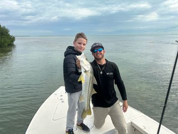 Two people on a boat proudly holding a large fish they caught.