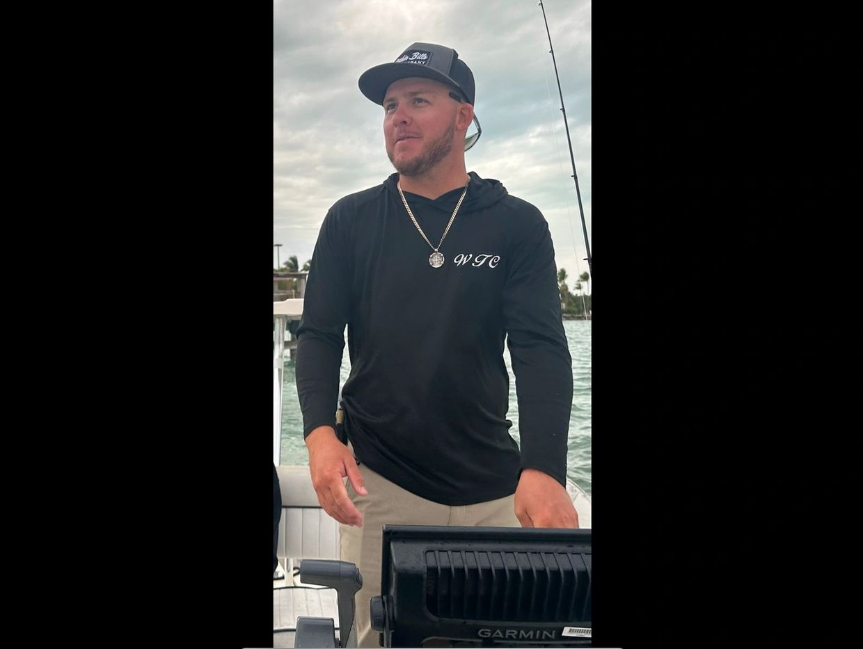 Man fishing on a boat wearing a black WTC hoodie and cap.
