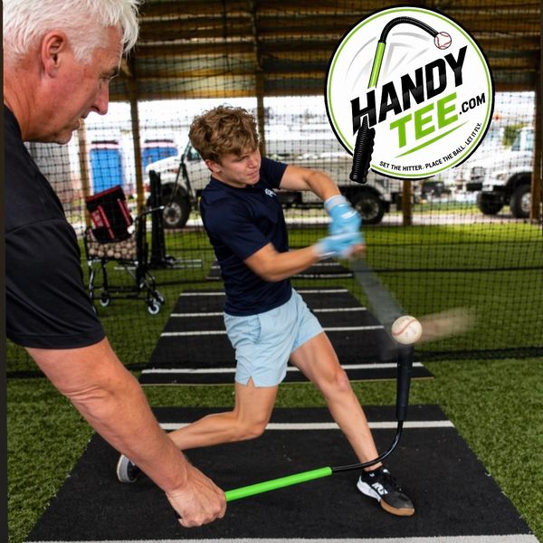 A young player hits a baseball off a Handy Tee while an older man assists.