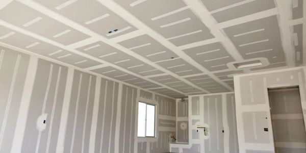 Interior room under construction with drywall installed on walls and ceiling.